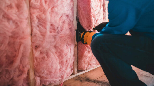 Worker installing batt insulation into wall framing cavity