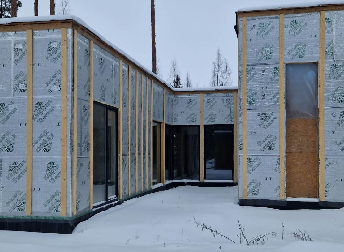Bedroom wing and entrance under construction in winter, with insulation boards, timber battens and installed windows.