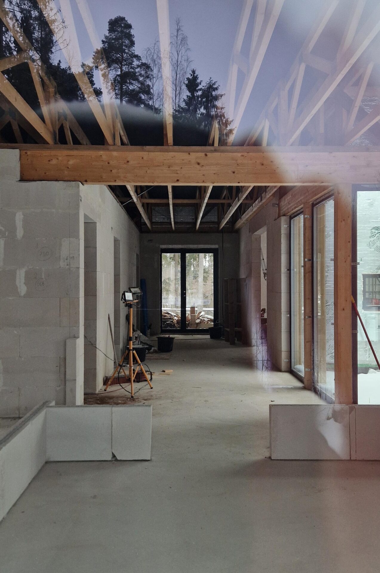 Long interior hallway during construction, with block walls, roof joists and a tall window at the far end.